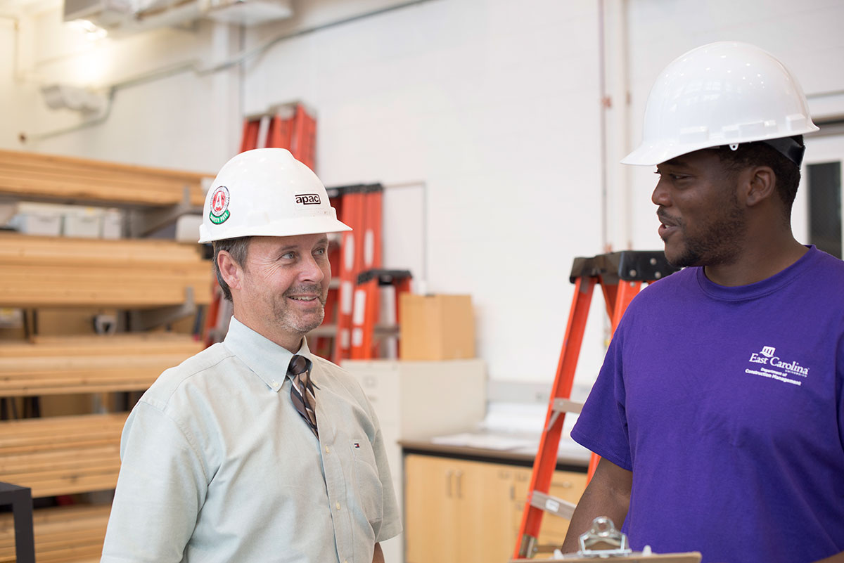 Mr. Wheeler stands with a student in their construction hats.